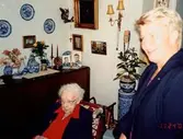 Greta Alm Andersson (född 1901, död 2005) firas på sin 100-årsdag i sin lägenhet på Brattåsgåren. Okänd kvinna till höger. Greta arbetade som småskollärarinna i Kållered 1928 - 1962 och var gift med Georg Andersson. Relaterat motiv: A1966.