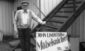 John Lindström (född 1902 i Lindome, död 1989 i Kållered) står utanför sitt snickeri på Gamla Riksvägen 79 (nu: Gamla Riksvägen 81), 1980-tal. På skylten står det 