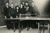 Kvinnor och män står samlade vid ett pingisbord, okänd plats 1930-tal. Från vänster: 1. Kurt Andreasson. 2. Erik Efraimsson. 3. Okänd. 4. Ulla Thalenius Roos. 5. Maj-Britt Pettersson. 6. Sven Svensson. 7. Thure Johansson Bjerrhede. 8. Harry Sjölin.