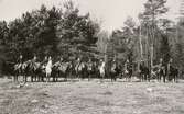 En grupp ryttare har ställt upp sig för fotografering på en äng. Runt 1900.