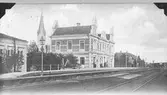 Järnvägsstationen i Falkenberg vid Mellersta Hallands järnväg som invides 1886. I bakgrunden syns tornet av kyrkan som stod klar 1892.