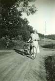 Ingrid Korneliusson Johansson (född 1940), Labacka, står med sin cykel på vägen till Tollered i Heljered, 1950-tal.