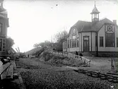 Omläggningsarbete av järnvägens sträckning söderut från Varberg. Fortfarande har inga broar byggts över klyftan mellan Platsarna och övriga staden. Den nya banan invigdes 1920. Bilden tagen mot söder med missisonskyrkan till höger, som ingivdes 1906. Vägen upp mot Platsarna finns ännu kvar. (Jämför med bild MR2_188.)