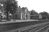 Exteriörbild av järnvägsstationen i Heberg med magasin, perrong parkbänkar och järnvägsspår.