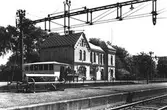 Exteriörbild av Tvååkers järnvägsstation och perrong från spårsidan. På perrongen står en parkbänk och stationen har fått en tillbyggnad. Fotot har använts till vykort.