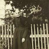 Emma Andersdotter Andersson (född 1854 i Landvetter, död 1931 i Livered) står vid ett staket, Livered 1:15 