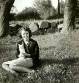 Ingrid Andersson (1918 - 2001, gift Skansing) sitter på gräsmattan hållandes en vit kattunge, Livered 1:15 