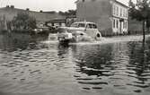 Översvämning på Linnégatan, Växjö, 1940. En bil plöjer fram, bakom den ser man några hus i kvarteret Dalen.