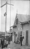 Köinge järnvägsstation som tillkom under första etappen av Falkenbergs järnväg, invigd 1894. På bänken invid stationen sitter en kvinna och bredivd henne står en ung man med käpp. Vid semaforen står en tågtjänsteman och i förgrunden ytterligare en tillsammans med en hund. Bildtext: 