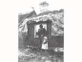 En piprökande man och en liten flicka står framför ett ovanligt stort fönster till en ryggåsstuga. Det är 