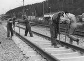 Utbyggnad för pendeltåget 11 april 1990. Vy norrut på män som utför utläggning av nya järnvägsspår, Torrekulla i Kållered. Till höger ses Långåsen samt fastigheter utefter Gamla Riksvägen.