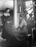 Kvinna i hemmiljö. Troligtvis fotografen Nanny Ekström till vänster och eventuellt en av hennes systrar till höger.