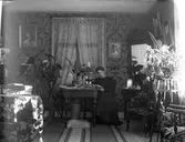 Kvinna vid bord i bostad. Personen på bilden är eventuellt syster till fotografen, Nanny Ekström.