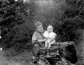 Kvinna och litet barn vid en vagn i en trädgård. Kvinnan på bilden är troligtvis bekant till fotografen.