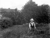 Troligtvis Anna Karin Zackrisson i trädgården vid fotoateljén på Mogärde. Anna Karin var dotter till fotografen Nannys syster Amy.
