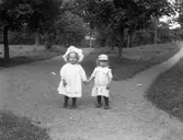 Två små barn i en trädgård eller park. Barnens anhöriga var troligtvis bekanta med fotografen.