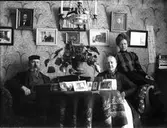 Tre personer i hemmiljö. Eventuellt är detta en bild på fotografen Nanny Ekström och hennes föräldrar, Johan och Christina.