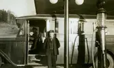 Två män (troligtvis chaufför John Johansson från Nygård) sitter i/vid en buss tillhörande Kållered bussbolag (Kålleredbussarna), 1930-tal. Den gick på linjen Göteborg-Anderstorp-Hällingsjö. Bussen står vid bensinstationen, nuvarande Streteredsvägen och Gamla Riksvägen, i Kållered centrum.
