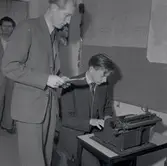 Herrar i kostym. En person vid en skrivmaskin i Godtemplargården, registrerar troligen  flyktingar ifrån Ungern. Hösten 56 - våren 57.