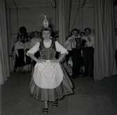 Ungerska flyktingar i Godtemplargården. Kvinna som dansar i traditionell romsk klädsel, en man i bakgrunden som spelar dragspel och folk som är publik. Hösten 56 - våren 57.