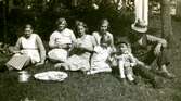 Vuxna och barn sitter tillsammans på gräsmattan och fikar, Kållered Stom 