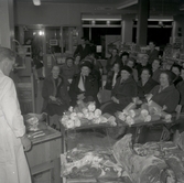 Man som styckar kött inför publik i en konsumbutik.