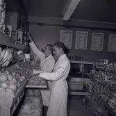 Två män i vita rockar i en konsumbutik.