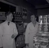 Två män i vita rockar i en konsumbutik.