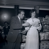 En man i kostym och en kvinna i vit rock i en konsumbutik.