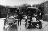 Två av de första droskbilarna (Taxi) som gick i trafik i staden på 1910-talet. Fotot är taget vid Västerbro och byggnaden t.h. är gamla varmbadhuset.