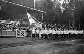 En kvinnlig gymastiktrupp marscherar in för uppvisning på idrottsplatsen i Ramnaparken på 1920-talet.