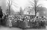 Skolavslutning utanför folkskolebyggnaden Centralskolan i Alingsås. Ett hundratal barn och några vuxna. På trappan står överlärare Karl Karlberg.