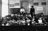 Kindergarten 1915 som låg på Österlånggatan (f.d. Sällfors Järnhandel). Lärarinnan i vit blus är Valborg Zetterwall-Bjönberg, assistenten heter Ruth Ögren.