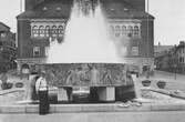 En man står vid fontänen Torgbrunnen på Stora Torget. Rådhuset i bakgrunden.