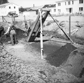 Två trädgårdsmästare skyfflar jord i en filtreringsanordning.