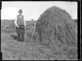 En man med redskap i hand bredvid en höstack, 1927.