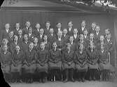 Konfirmandfotografi med prästen i mitten. Alla bär svarta kläder; flickorna bär även svarta handskar. Bytet till vit klädsel skedde från 1910-talets mitt.
(Sannolikt taget i Björkströms ateljé på Torggatan i Varberg, se bild GB1_1028)
(Negativet skadat i vänstra hörnen)