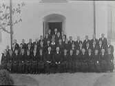 Konfirmandklass i svarta kläder med prästen vid kyrkdörren. Flickorna bär även svarta handskar. Bytet till vit klädsel skedde från 1910-talets mitt.