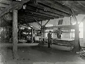 Interiör från garveri med remdrift till maskinerna. En arbetare står vi ena maskinen.
