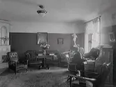Interiör av salongen i bostaden på andra våning av Apoteket Kronan i huset vid hörnet Torggatan-Drottninggatan, Varberg. Apotekare Hultkvist sitter vid sin sekretär. Kv Apotekaren 8.