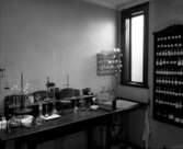 Apoteket Kronans laboratorium, kv Apotekaren 8. Bord med vågar, pipetter, kolvar, mortlar och annat en apotekare behövde för att bereda olika läkemedel. Vägghyllan till höger är fylld med etikettförsedda småflaskor med olika ingredienser för tillverkningen.