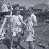 Tennisfinaler och prisutdelning en måndag. Två tennisspelare och en pojke vid domarplatsen till vänster.