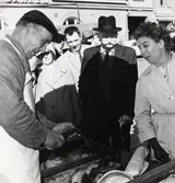 Albert Johansson, fiskhandlare i Ingemanssons fiskaffär, Växjö, servar kunder på Stortorget i Växjö 1962.
I bakgrunden skymtar Skånska bankens fastighet vid Kungsgatan.