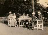 Från vänster ses Bibbi Björck sittandes i knät på en dam, på bänken Laila Björck med dottern Ulla samt även Lailas far.

Fotografi taget i juni 1929 vid sommarbostaden Strandlyckan vid Landvettersjön, Slamby 1:4 i Landvetter socken. Huset övertogs senare av Stiftelsen Enandergården, Härlanda församling, på 1950-talet.