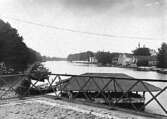 Vy mot söder över Lidan.
Fotografiet visar sköljflotten vid körbron i Lidköping.
Skorstenarna i bakgrunden tillhör bryggeriet Örnen.