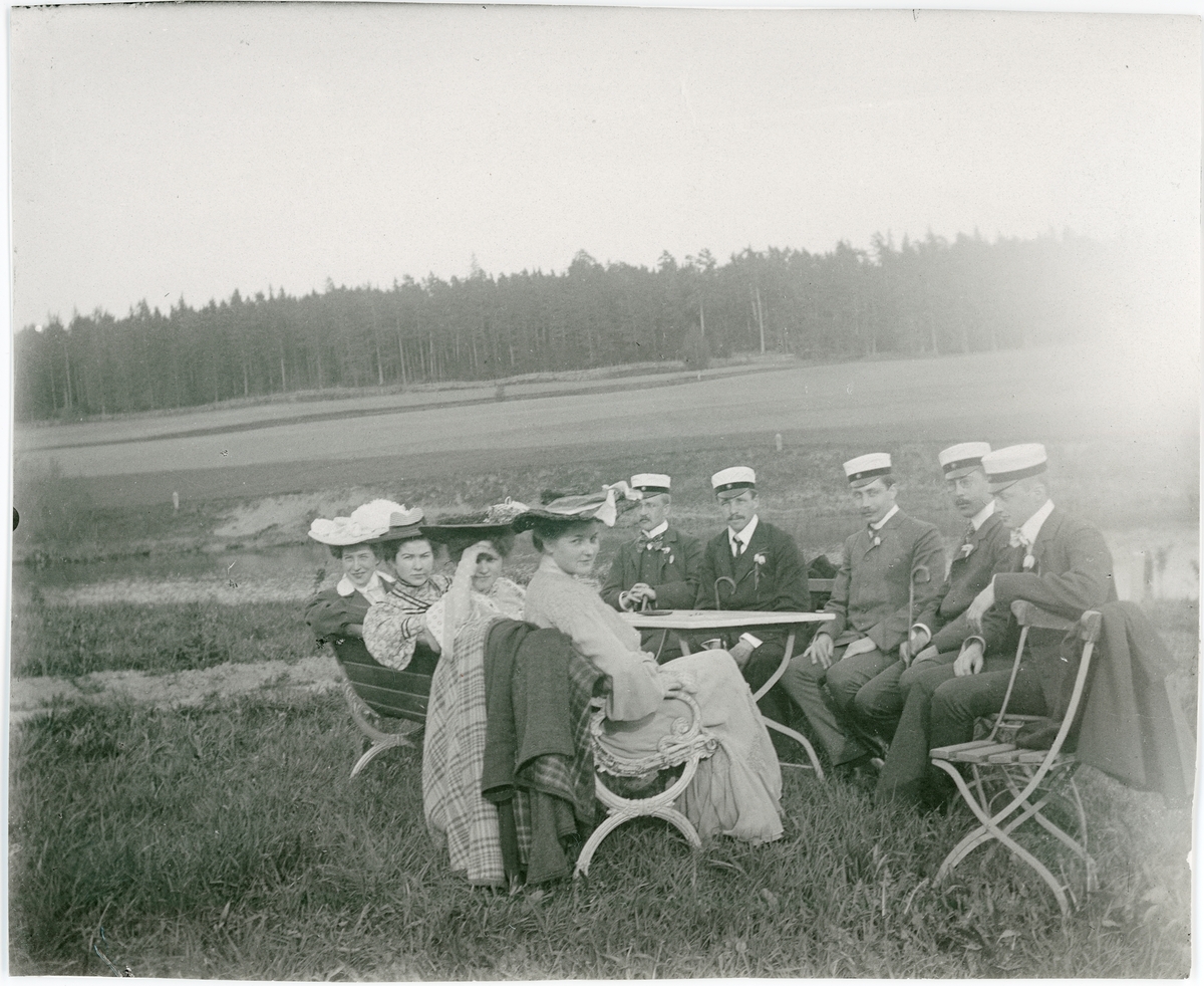 Okänd,, Students, women and men sitting at table outside on grass, forest in the background, likely Uppland around 1900