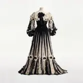 Tvådelad spets- och tyllklänning monterad på docka. NK:s Franska damskrädderi. Svart och vit klänning med spetskrage, dekorerad med svarta sammetsband och paljetter i guld och svart. Beställd av Blanche Bonde (född Dickson) gift med greve Carl Bonde. Stamkund med stor modegarderob. Levererad 1904. Göteborgs stadsmuseum. GM:22458.