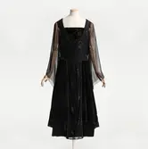 Klänning, monterad på docka, av siden och sammet med chiffongärmar och gnistrande pärlbroderier i form av spindelväv, möjligen efter ett original från Madeleine Vionnet. Beställd av Irma Rosenbaum född Pettersson (1886-1976) från NK:s Franska damskrädderi, levererad ca 1919.
23_Uppropet 13, detaljbild NK_23_Detalj2. KOMPLETTERAS