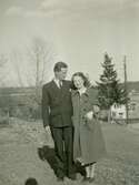 Björn Ekman (1913 - 1992) och Mary Ekdahl (1920 - 1988, gift Ekman) står i Labacka vid Missionskyrkan (senare Ekenkyrkan), 1 maj 1941. Till höger ses bröderna Magnussons bostäder 