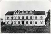 Norrtullskolan i Växjö, 1882. 
Framför byggnaden syns monumentet över domprosten Håkan Sjögren (1727-1815), Växjö.